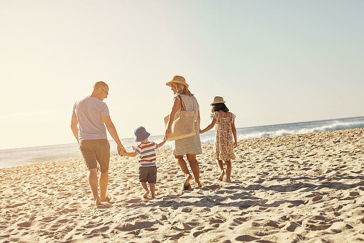 Famille marchant sur le sable au bord de la mer pendant les vacances d’été, moment complice et nature.