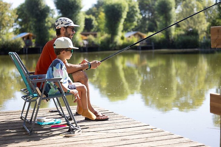 Père et enfant pêchant à l’étang d’un camping nature, moment calme en pleine nature bénéfique pour le bien-être.