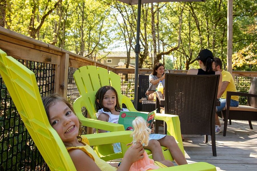 Enfants détendus sur la terrasse d’un mobil-home, ambiance conviviale pour un camping dernière minute août en famille.
