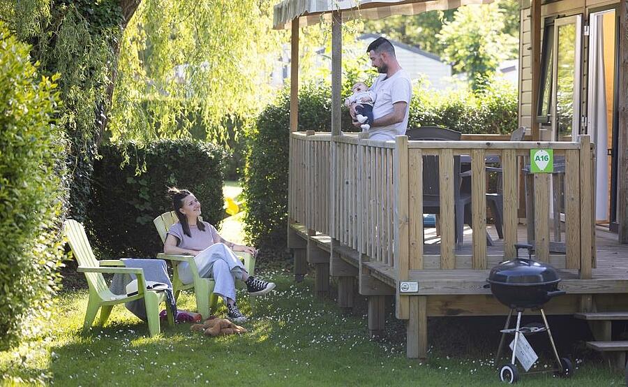 Une famille se détend devant un mobil-home dans un camping du Calvados, entourée de verdure, offrant un cadre paisible et confortable pour des vacances en Normandie.