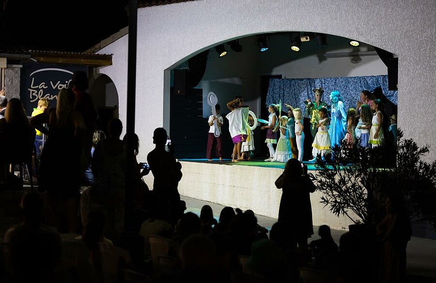 Enfants sur scène lors d’un spectacle en camping, familles réunies pour une animation conviviale et libre en soirée.