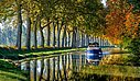 Une péniche naviguant paisiblement sur le Canal du Midi bordé d’arbres, un cadre naturel idéal à proximité des campings Sites et Paysages.
