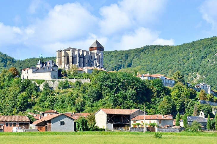 Vue du village de Saint-Bertrand-de-Comminges avec sa basilique majestueuse, nichée sur une colline verdoyante face aux Pyrénées.
